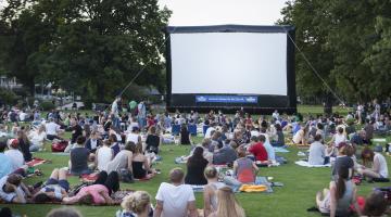 People sat around on picnic blankets outside watching an outdoor cinema screen